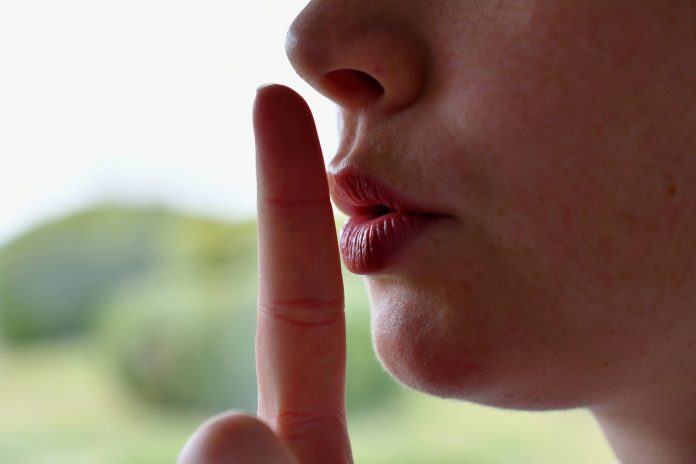 Close-up of a child pressing a finger to the lips in a shushing gesture, signaling quiet